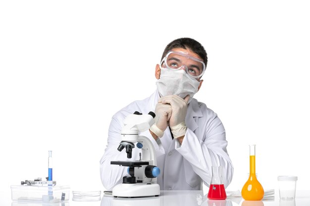 Front view male doctor in white medical suit with mask due to covid sitting on a white space