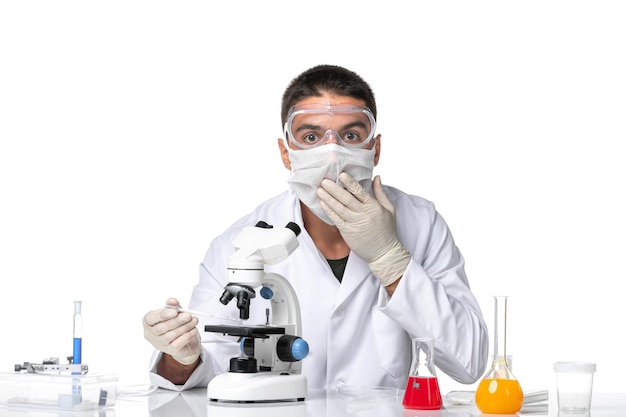 밝은 공백에 현미경을 사용하여 covid로 인해 마스크가있는 흰색 의료 소송에서 전면보기 남성 의사