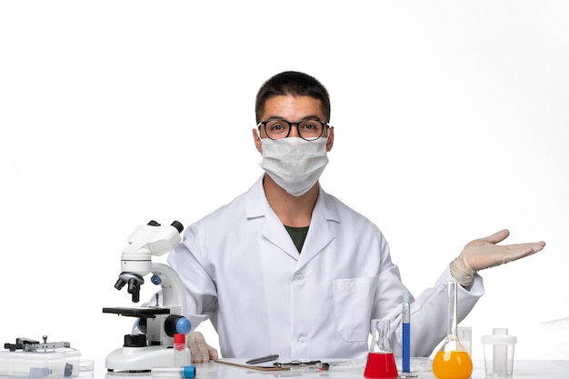 Вид спереди мужчина-врач в белом медицинском костюме с маской из-за covid на белом столе