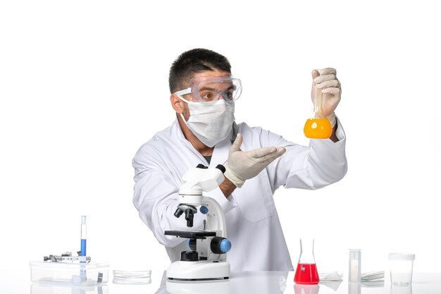 Вид спереди мужчина-врач в белом медицинском костюме с маской из-за covid, работающего с растворами на белом пространстве
