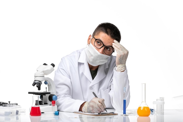 Front view male doctor in white medical suit with mask due to covid writing on a white space