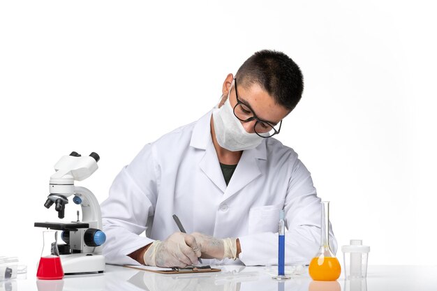 Front view male doctor in white medical suit with mask due to covid writing on a white space