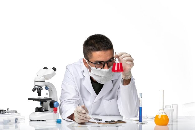 Front view male doctor in white medical suit and with mask working with solution on light-white space