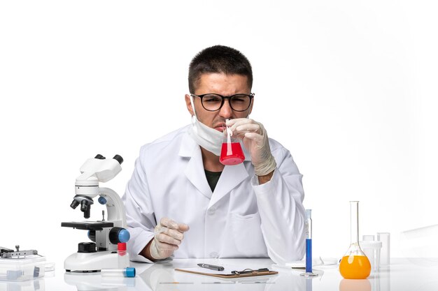 Front view male doctor in white medical suit and with mask working with solution on light white space