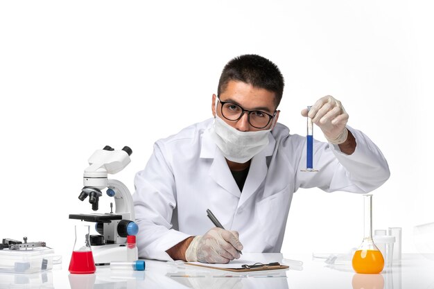 Front view male doctor in white medical suit and with mask working with solution on white space