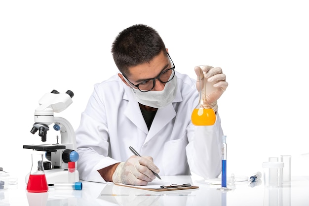 Front view male doctor in white medical suit and with mask working with solutions on white space