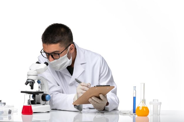 Front view male doctor in white medical suit working with microscope on a white space