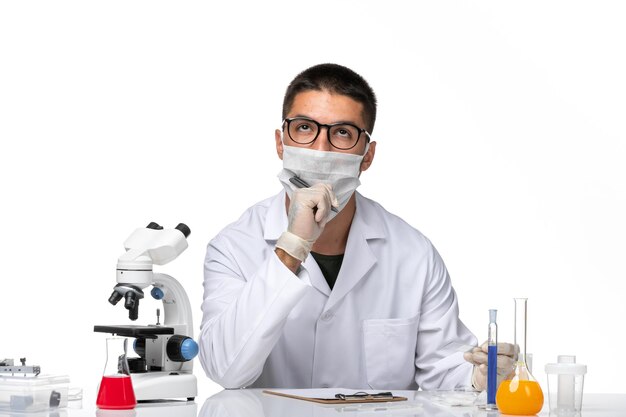 Вид спереди мужчина-врач в белом медицинском костюме, работающий с растворами на светлом белом пространстве