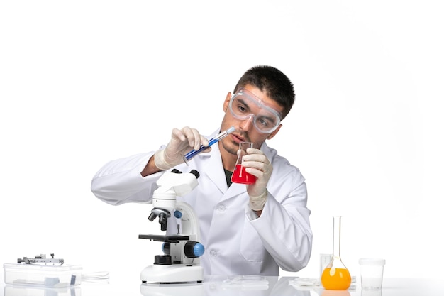 Front view male doctor in white medical suit working with solutions on white desk