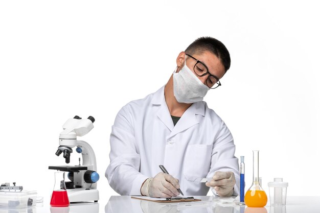 Front view male doctor in white medical suit working and writing on a light-white space