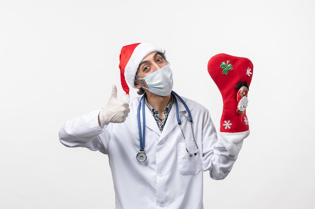 白い壁のウイルスcovid-クリスマスに大きな休日の靴下を持つ正面図の男性医師