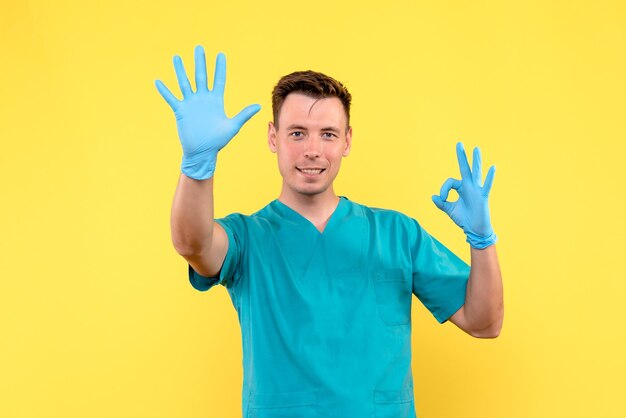 Front view of male doctor with blue gloves on yellow wall