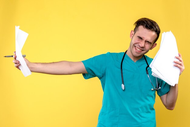 Front view of male doctor with documents on a yellow wall