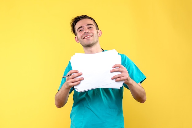 Front view of male doctor with documents on yellow wall