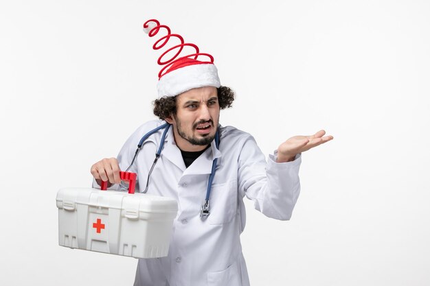 Front view of male doctor with first aid kit on a white wall