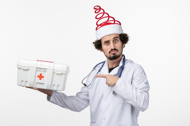 Front view of male doctor with first aid kit on white wall