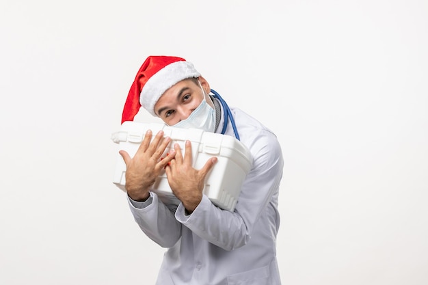 Front view of male doctor with first aid kit on white wall