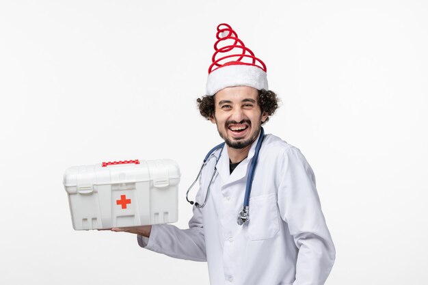 Front view of male doctor with first aid kit on white wall