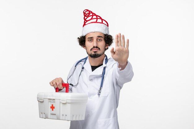 Front view of male doctor with first aid kit on white wall