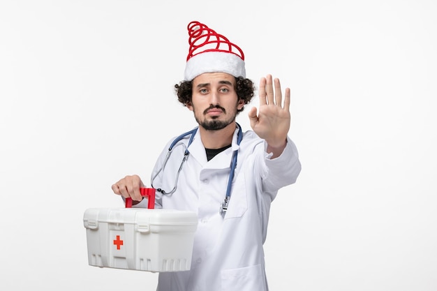 Front view of male doctor with first aid kit on white wall