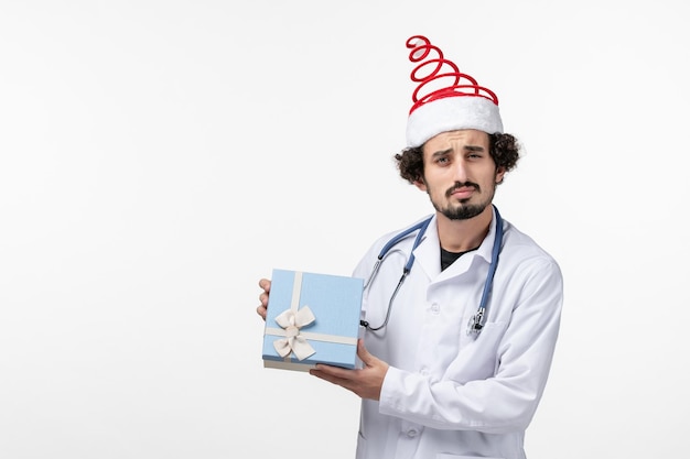 Front view of male doctor with holiday gift on white wall