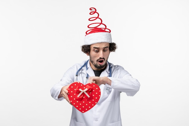 Vista frontale del medico maschio con regalo di festa sul muro bianco