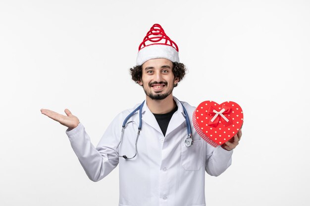 Front view of male doctor with holiday present on a white wall