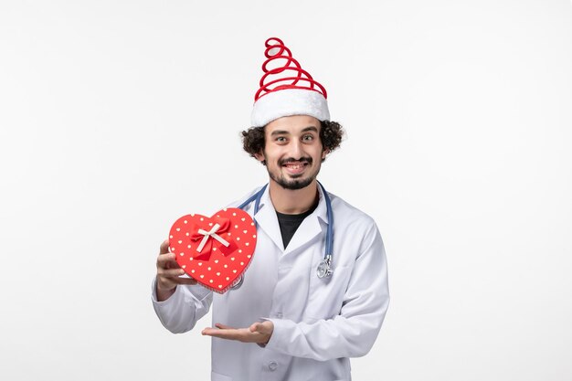 Front view of male doctor with holiday present on a white wall