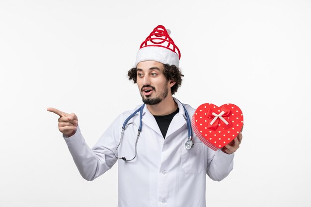 Front view of male doctor with holiday present on the white wall