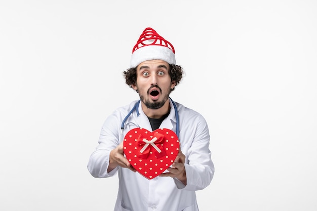 Front view of male doctor with holiday present on white wall