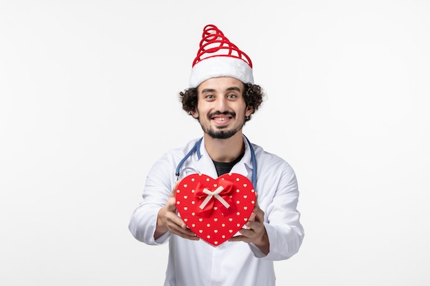 Front view of male doctor with holiday present on white wall