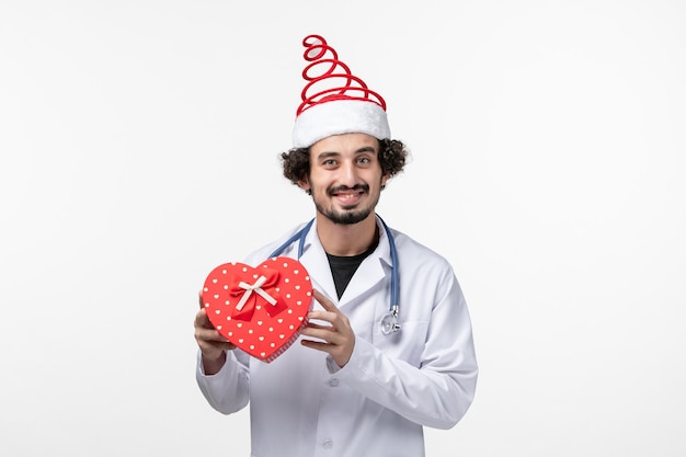 Front view of male doctor with holiday present on white wall