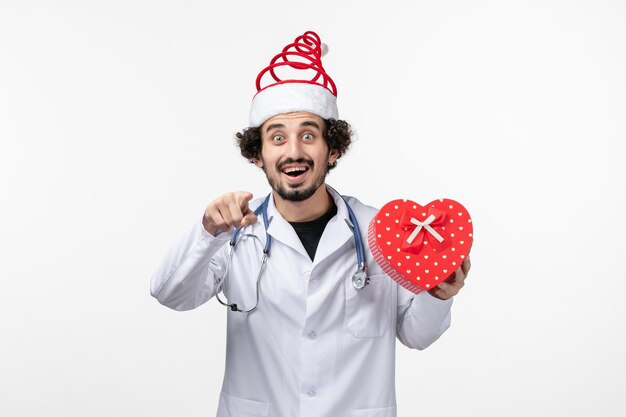 Front view of male doctor with holiday present on white wall