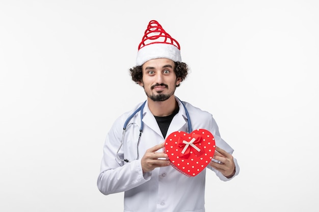 Вид спереди мужского врача с праздничным подарком на белой стене