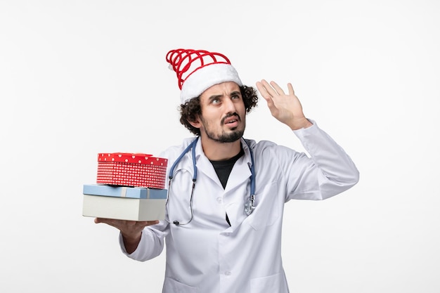 Front view of male doctor with holiday presents on white wall
