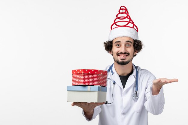 Front view of male doctor with holiday presents on white wall