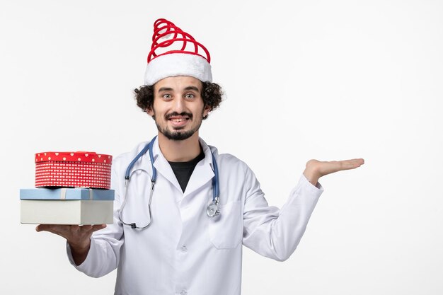 Вид спереди мужского врача с праздничными подарками на белой стене