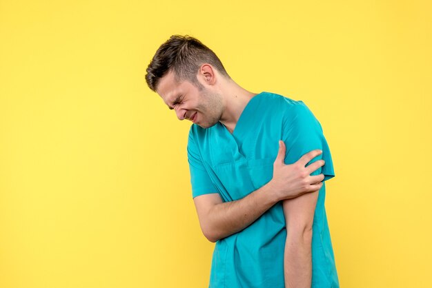 Вид спереди мужского врача с больной рукой на желтой стене