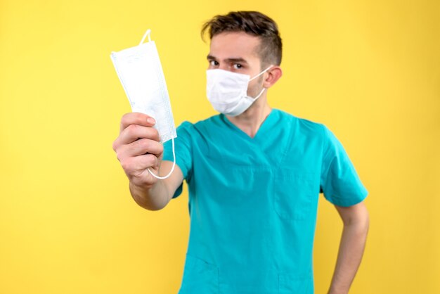 Front view of male doctor with mask on a yellow wall