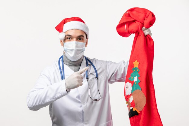 Front view of male doctor with present bag on a white wall