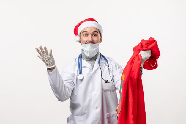 Front view of male doctor with present bag on white wall