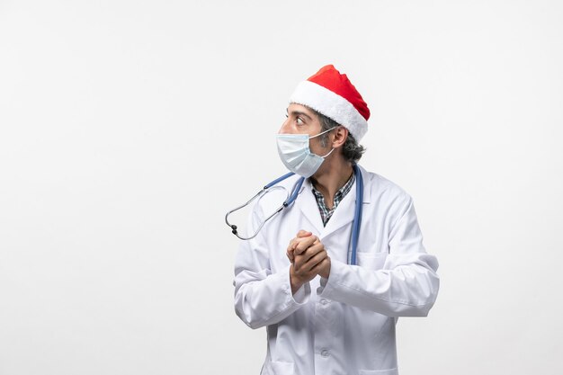 Front view male doctor with red cap and mask on a white wall new year covid pandemic