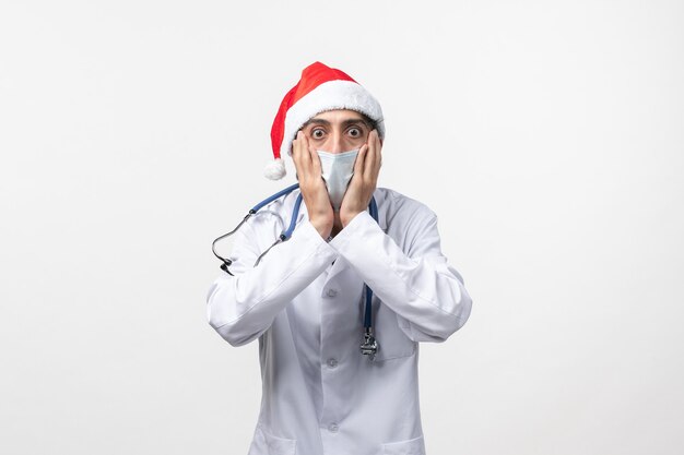 Front view male doctor with red cap and mask on the white wall new year covid pandemic