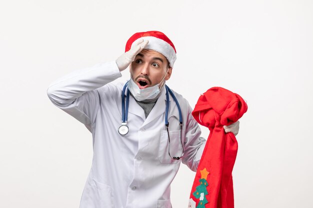 Front view of male doctor with red present bag on white wall