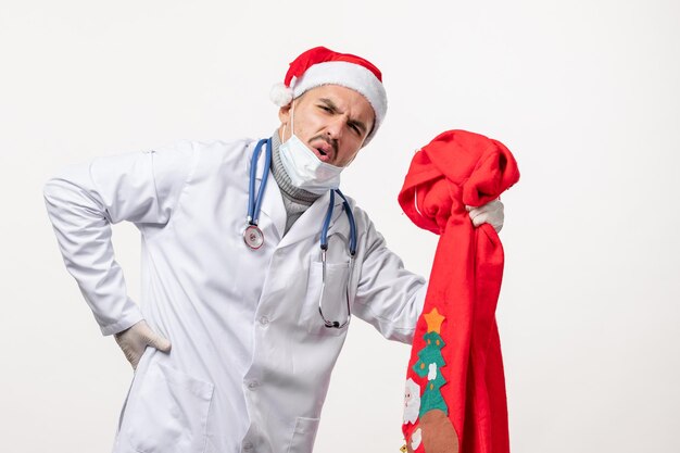 Front view of male doctor with red present bag on white wall