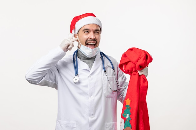 Front view of male doctor with red present bag on white wall