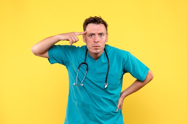 Front view of male doctor with serious expression on yellow wall
