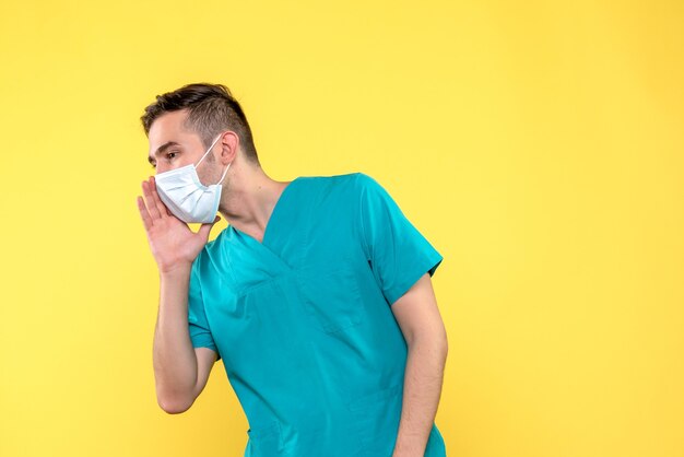 Front view of male doctor with sterile mask on a yellow wall