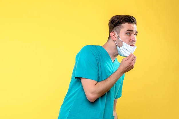 Front view of male doctor with sterile mask on yellow wall
