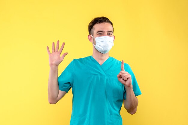 Front view of male doctor with sterile mask on yellow wall